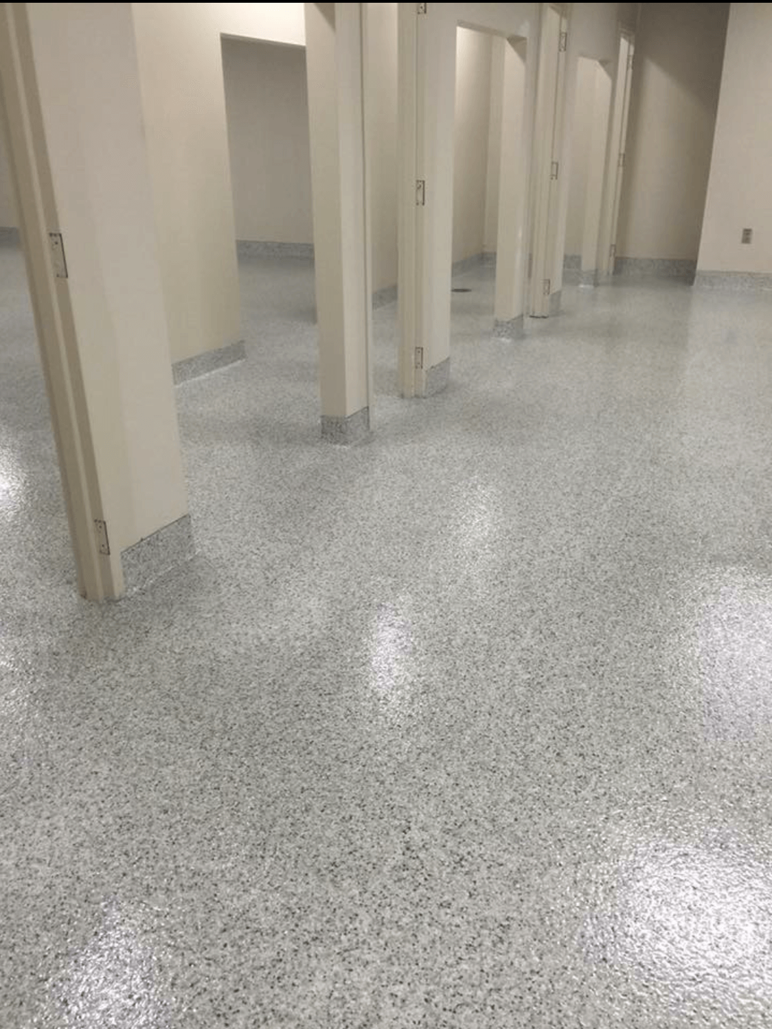 A bathroom with a row of stalls and a shiny floor.