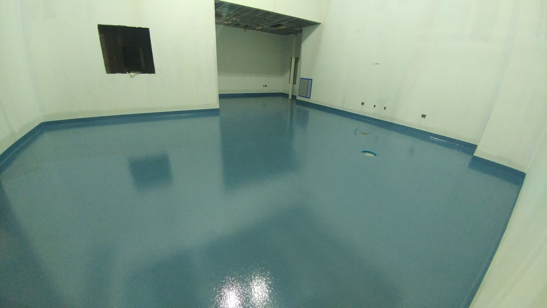 Blue-floored room with white walls and a rectangular window. A doorway is visible in the back.
