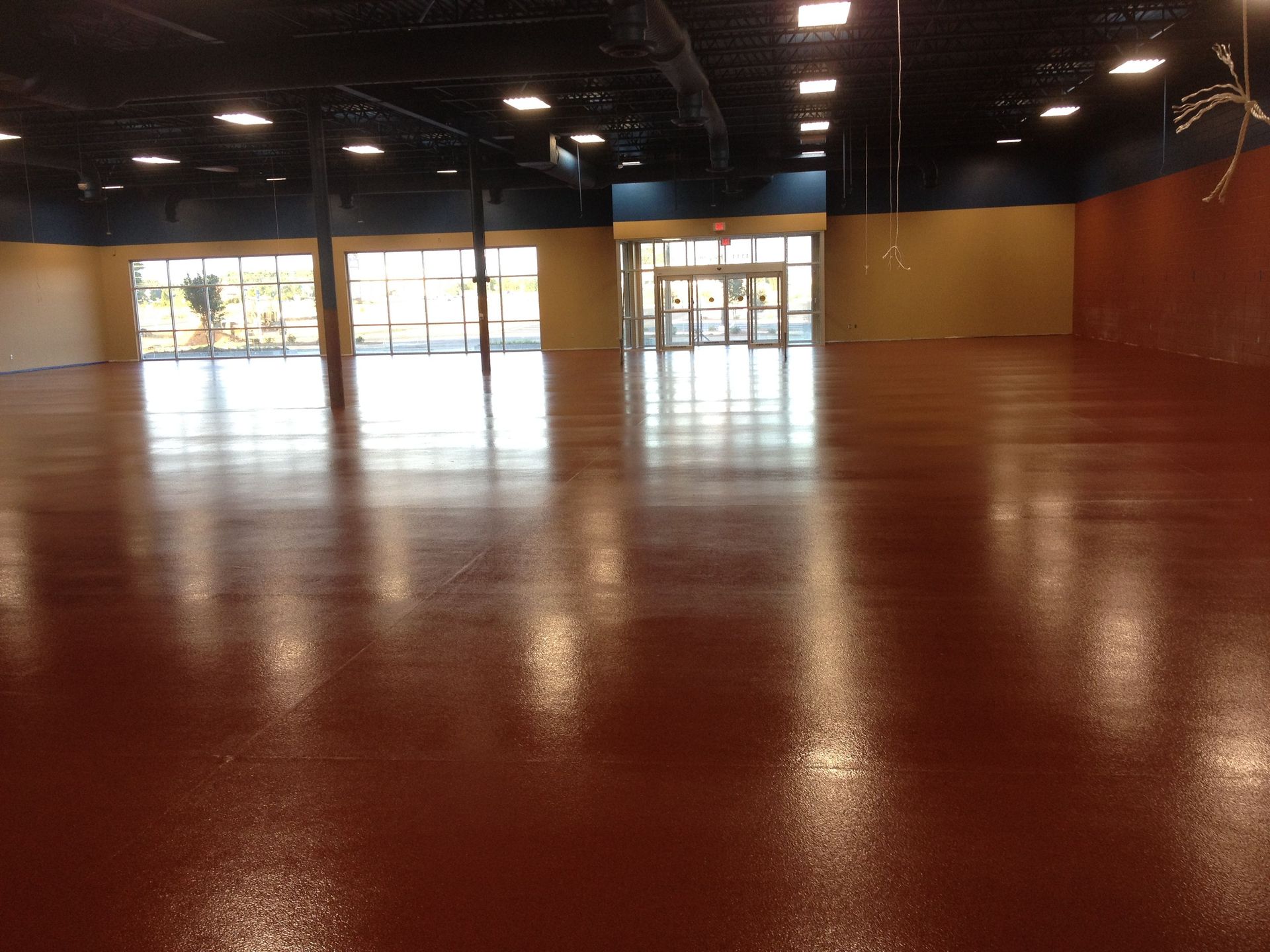 Empty commercial space with a shiny, reddish-brown floor and large windows in the distance.