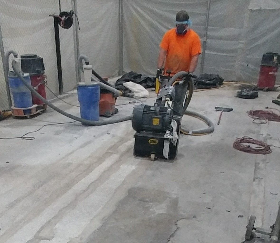 A man wearing a mask is using a machine on a concrete floor.