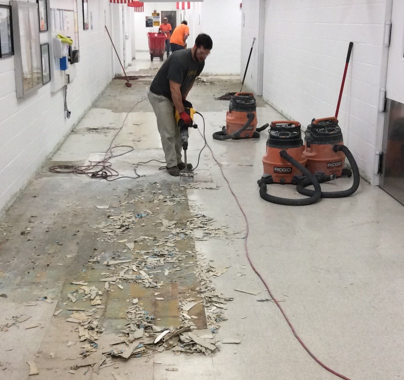 A man is using a drill to remove a tile floor in a hallway