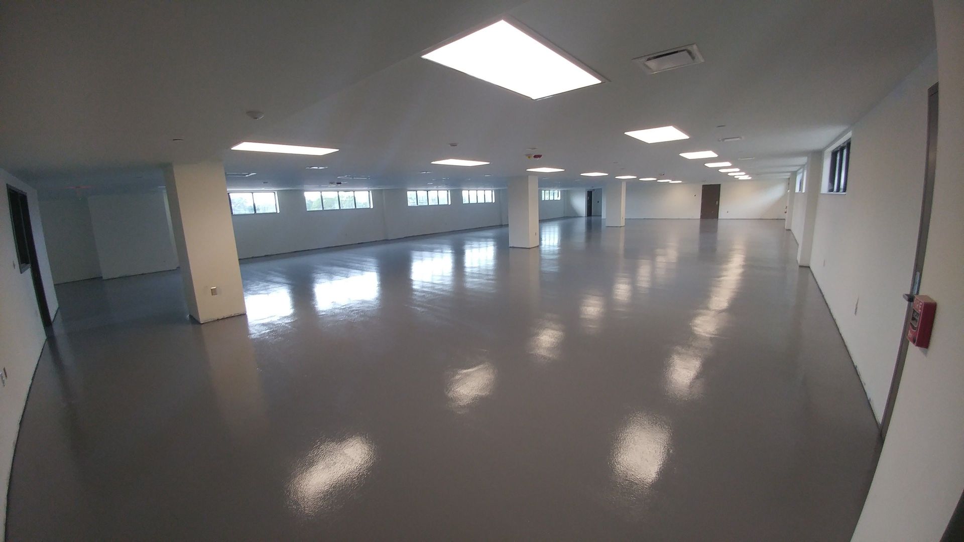 Wide, empty room with glossy gray floor, recessed lighting, and windows along one wall.