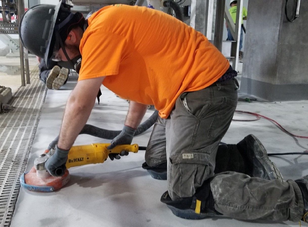 A man is kneeling down using a grinder on the floor.