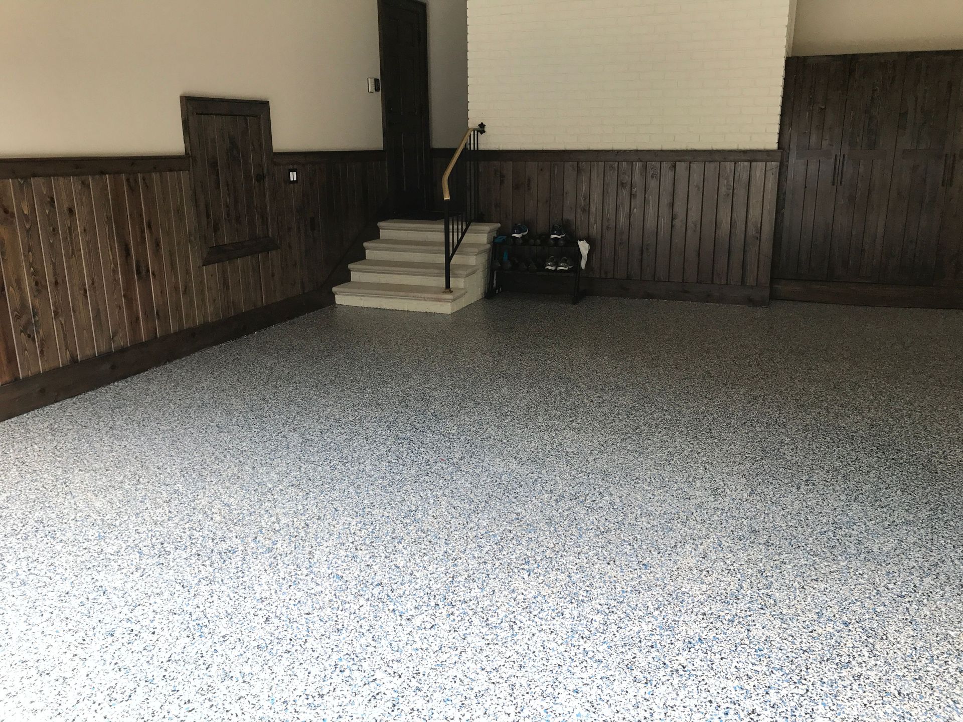 Garage interior with gray speckled floor, dark wood paneling, and stairs leading up.
