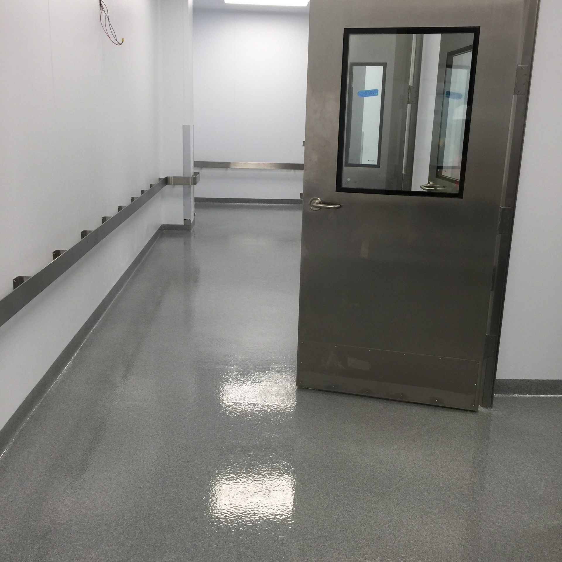 Clean hallway with gray flooring, metal door with window, and white walls.