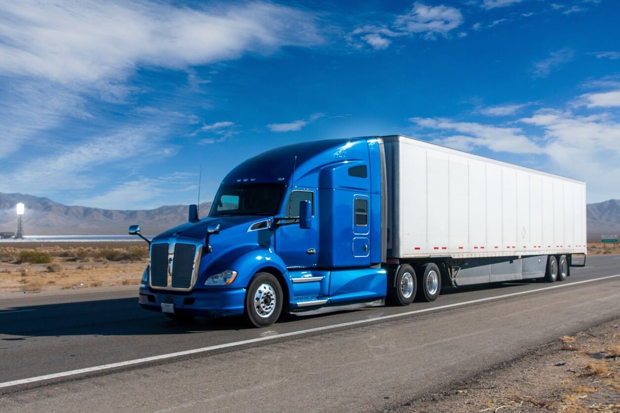 A blue semi truck with a white trailer is driving down a highway.