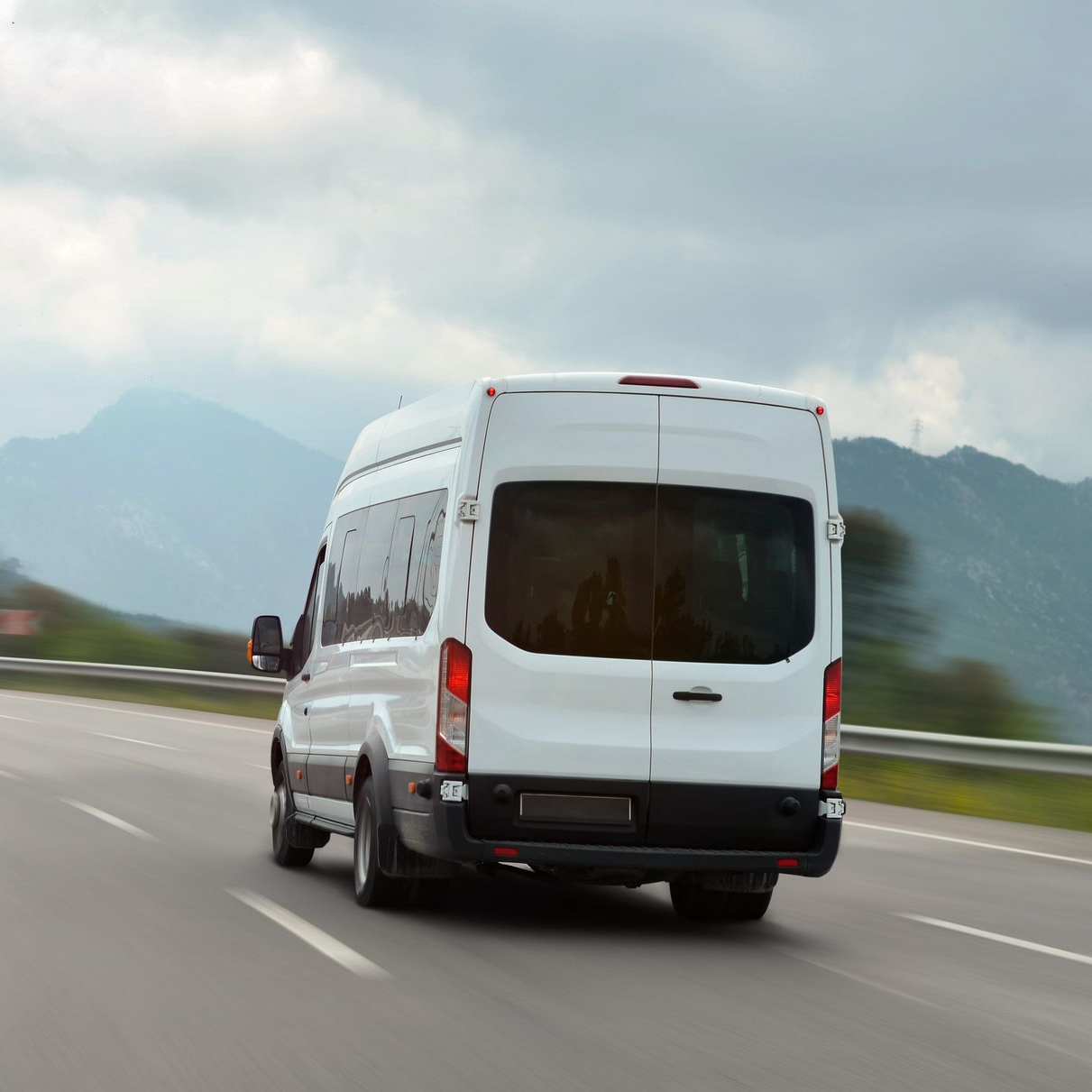 White van driving on a curving highway with mountains in the distance at sunrise
