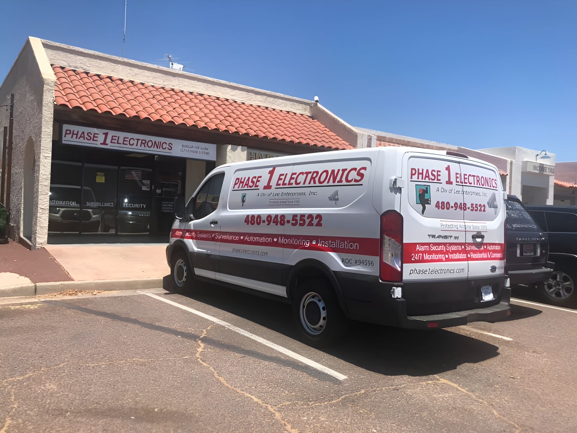 Plumber & Electronics service van parked outside a storefront in a sunny lot