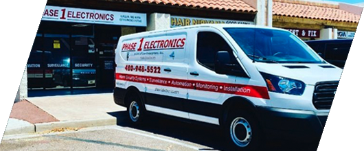 Electronics store storefront with a white van parked outside, showing business signage and red stripes.