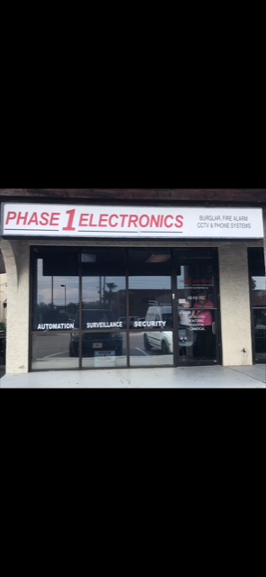 Storefront with a “PHASE 1 ELECTRONICS” sign and glass windows showing electronics inside.