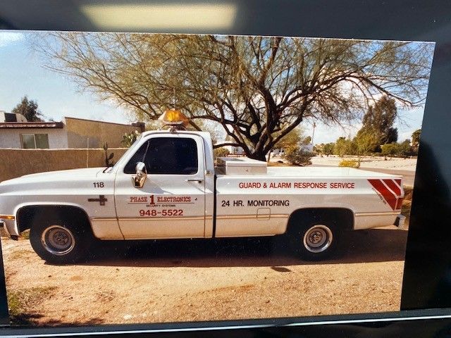 White towing truck parked on dirt road under a tree, with business lettering on the side.