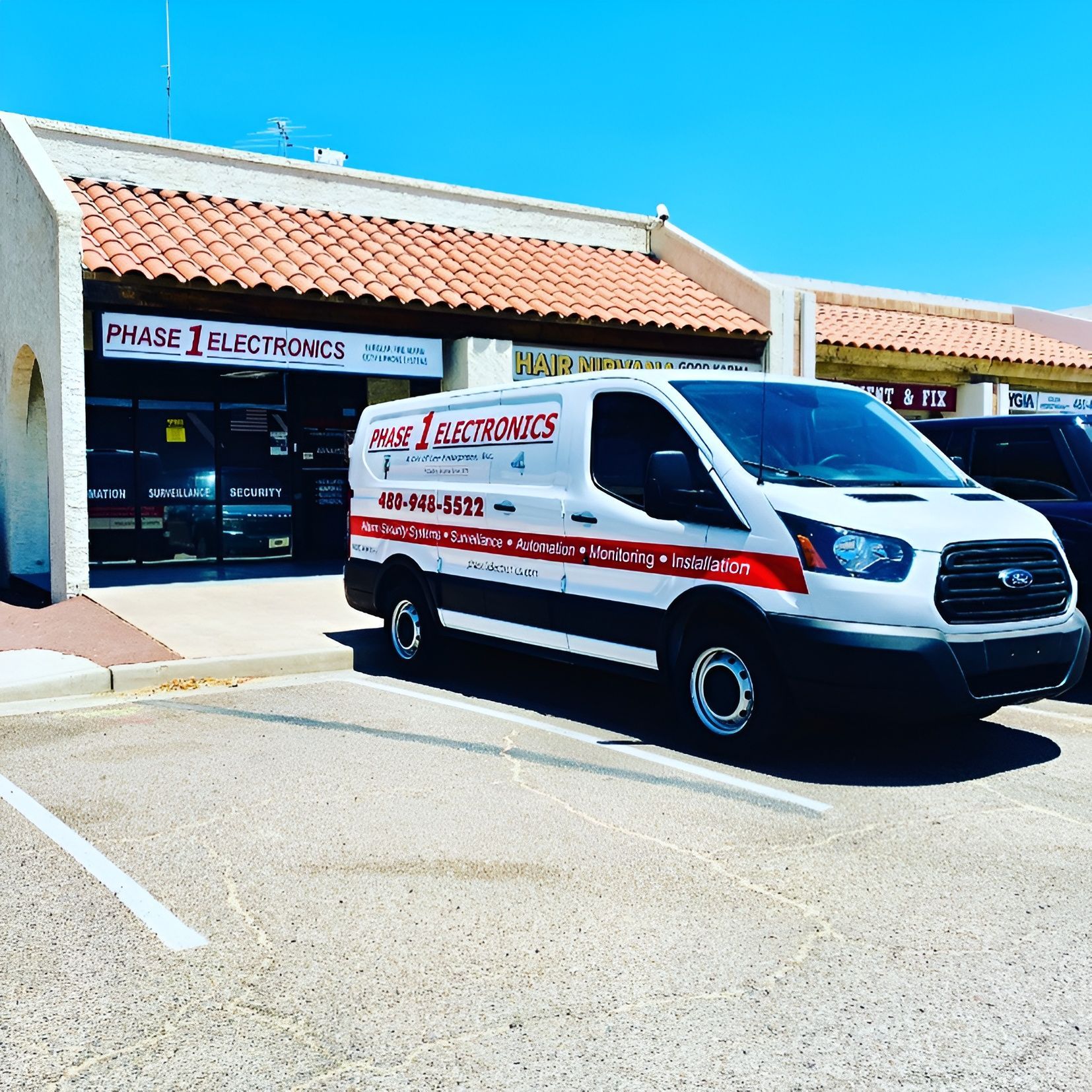 White Phase I Electronics service van parked outside a storefront on a sunny day
