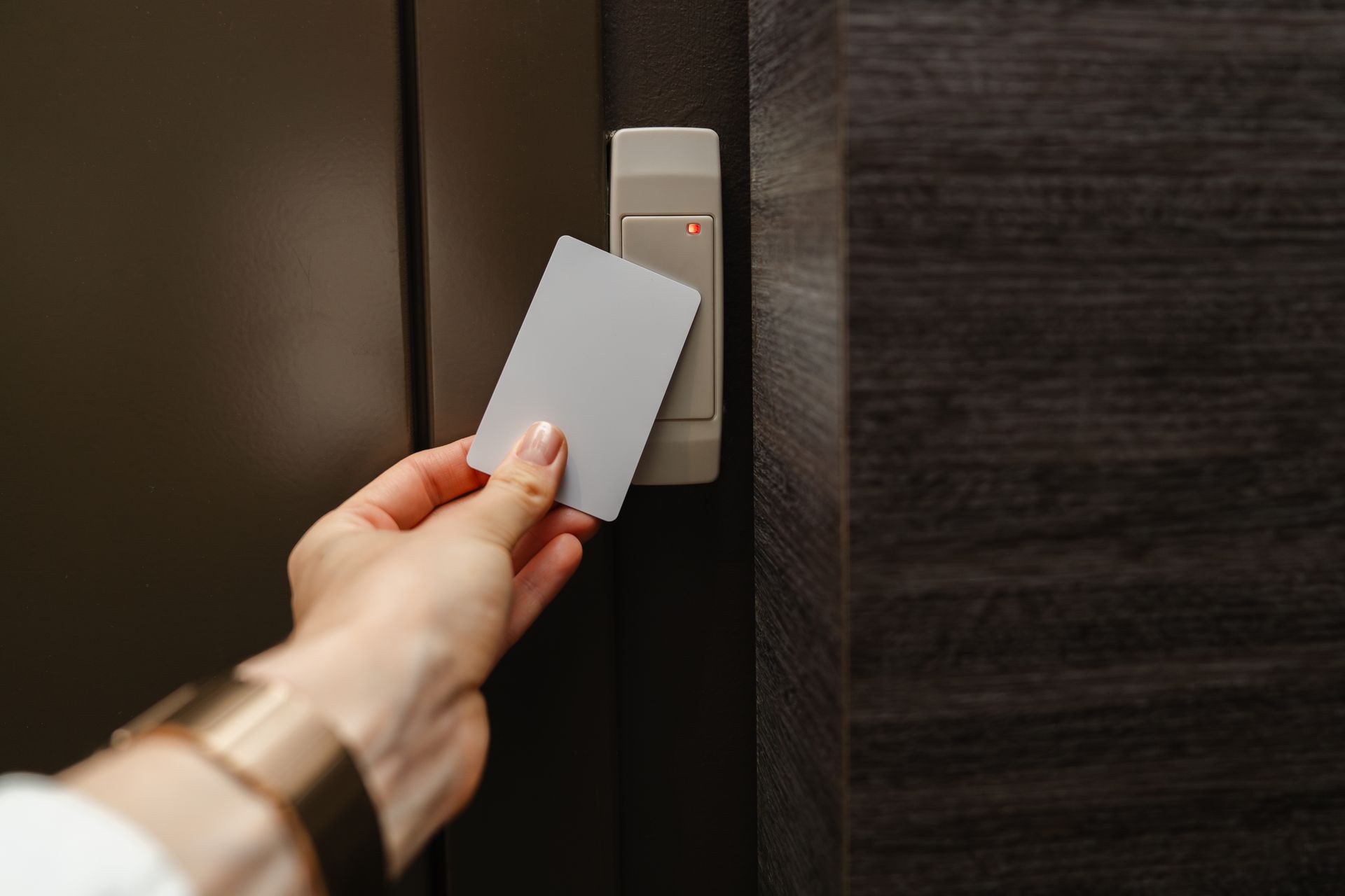 Hand holding a white key card near a door lock reader