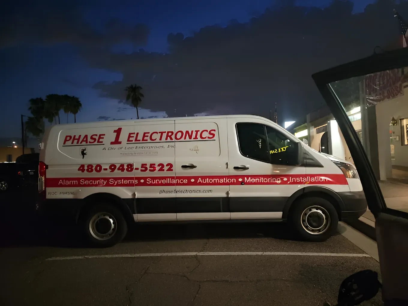 White Phase 1 Electronics van parked at dusk, with red logo and phone number on the side.