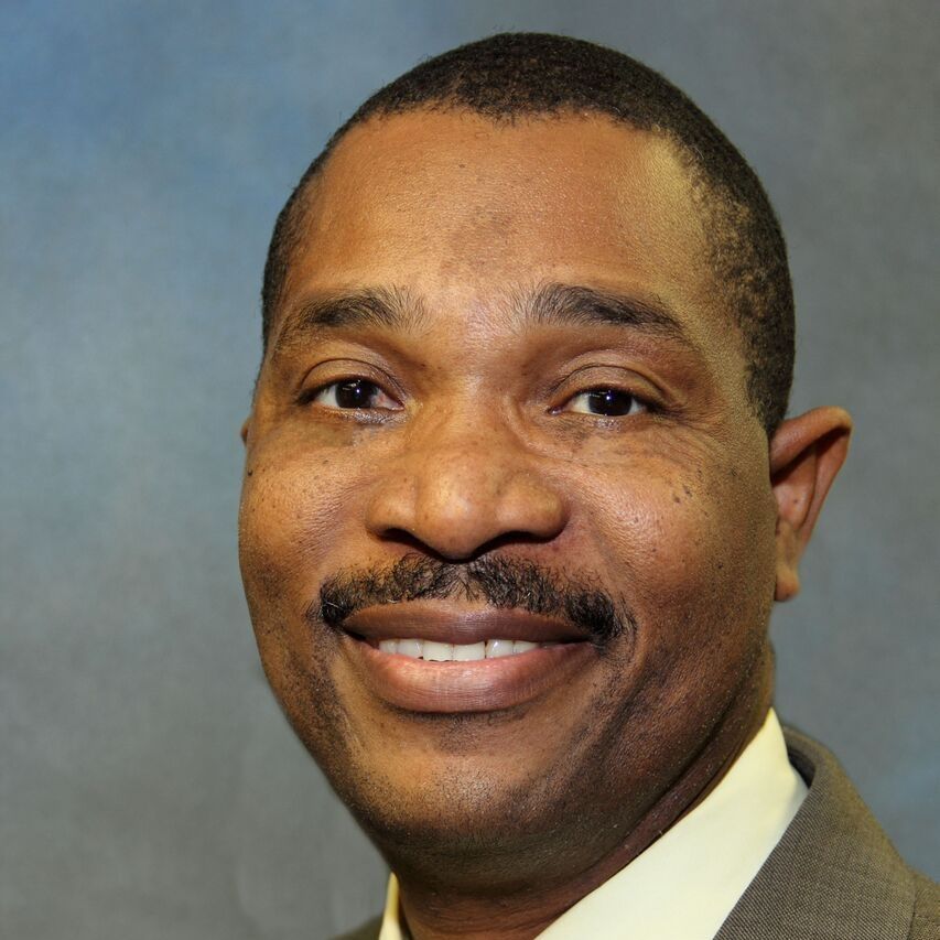 Smiling man in a suit and tie against a plain gray background