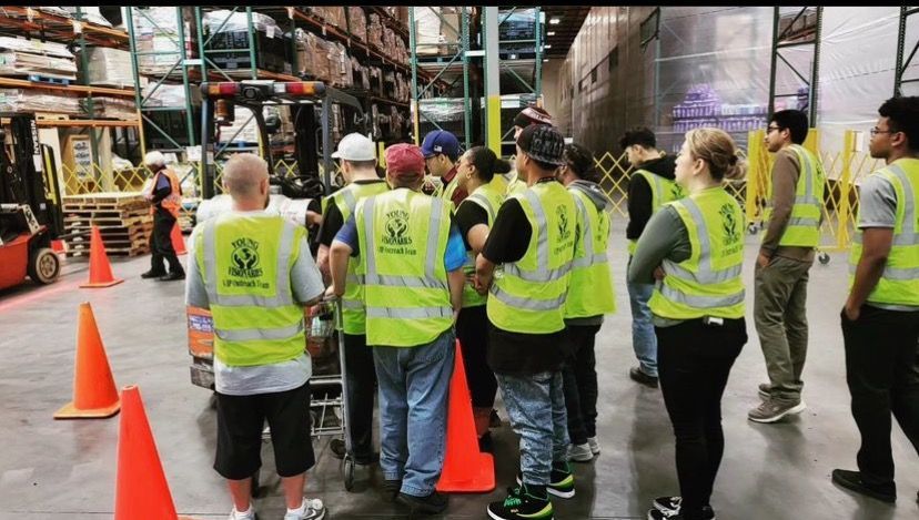 Group of workers in neon safety vests standing by orange cones in a warehouse aisle