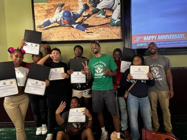 Group of people holding certificates in a celebratory indoor gathering under a “Happy Anniversary” banner