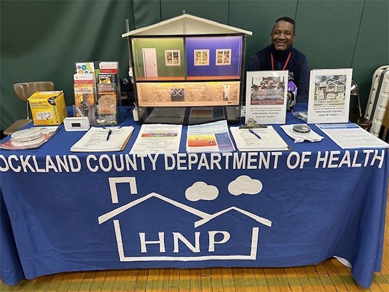 Rockland County Health Department booth with informational brochures, a display house, and a smiling staff member