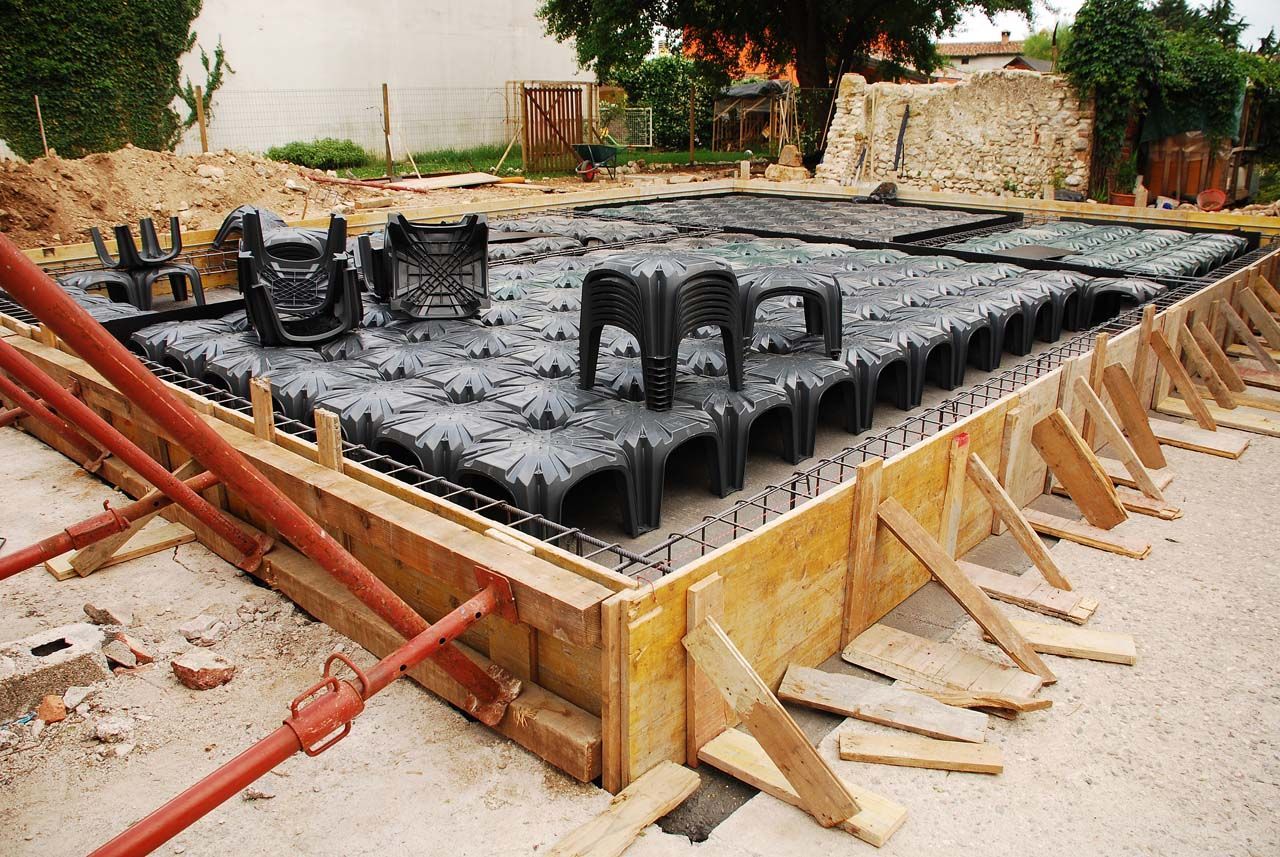 Concrete foundation under construction with black plastic void forms and wooden bracing around the edges