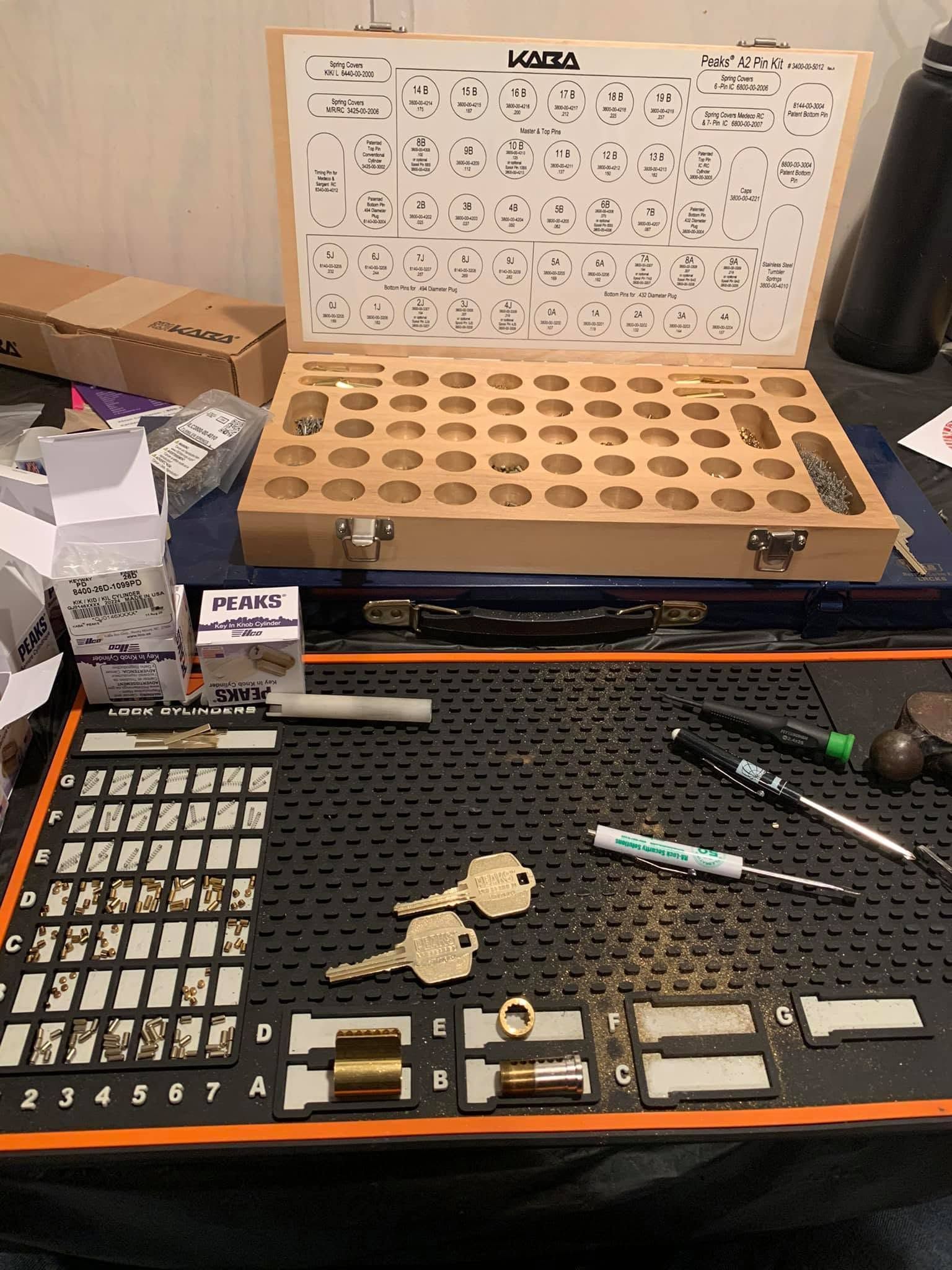 Open toolkit with organized small parts, tools, and a parts chart on a black work mat.