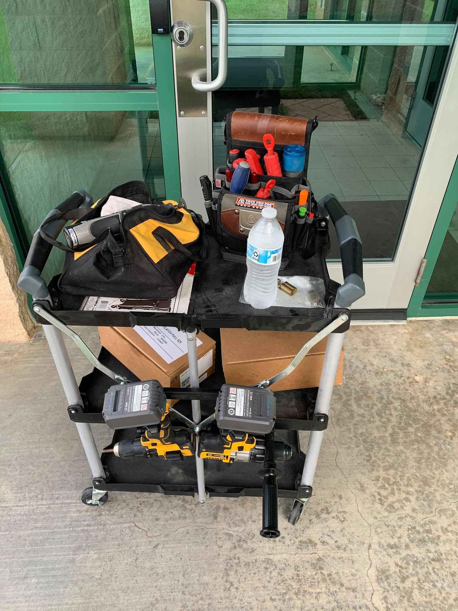 Two-tier cart with tools, bags, and water bottle in front of glass doors