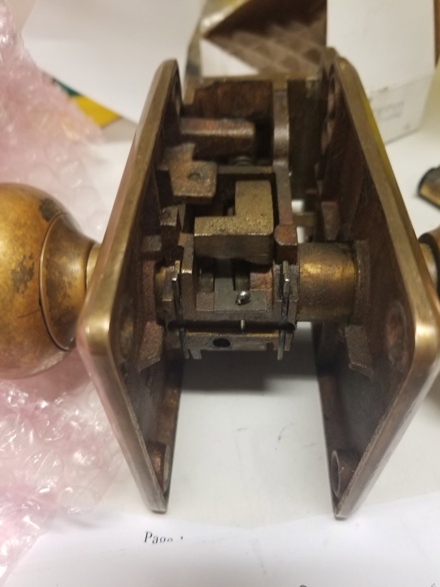 Close-up of a brass door lock mechanism with exposed internal parts on a white surface