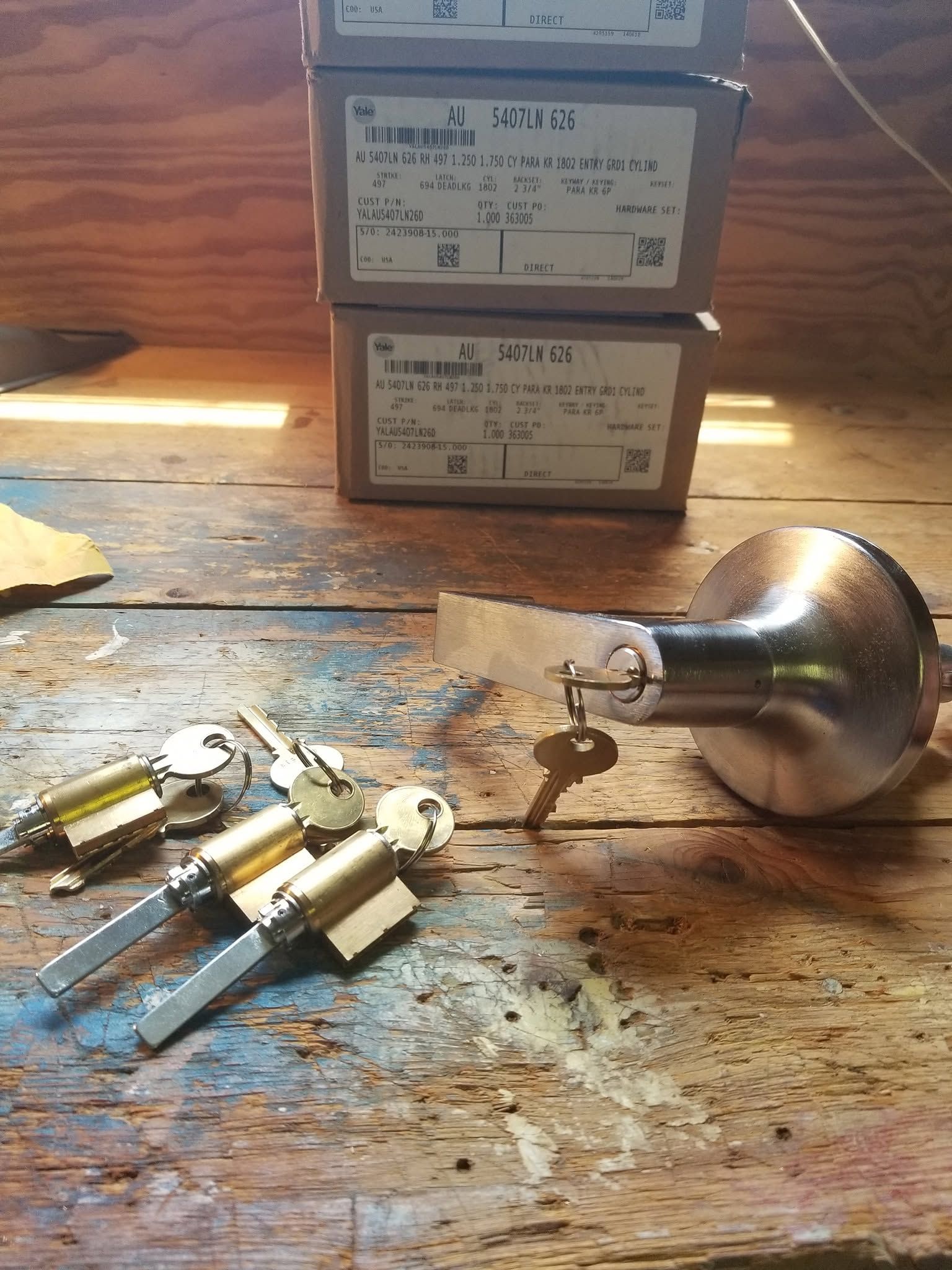 Brass door locks and keys on a worn wooden workbench with two stacked product boxes in the background