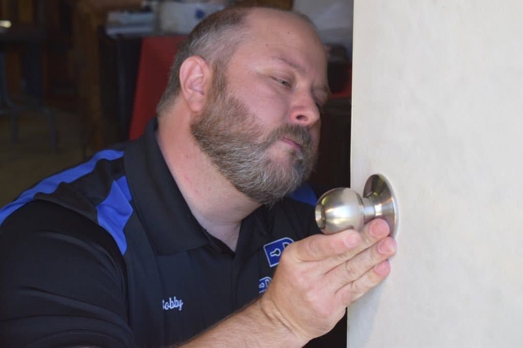Man holding a silver door knob up to his nose and examining it closely indoors