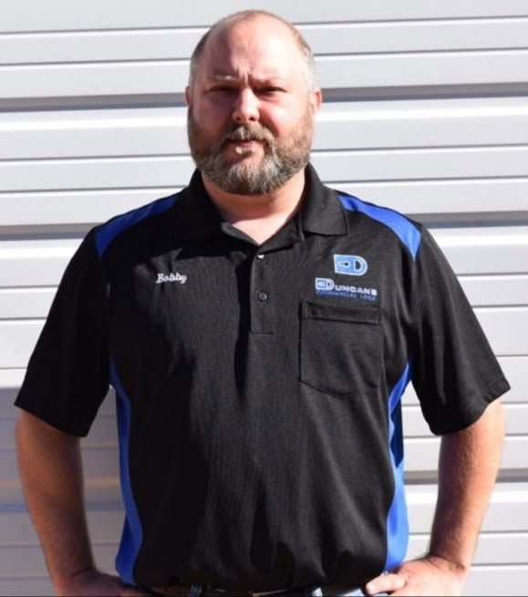 Man standing in a black and blue polo shirt against a white garage door.