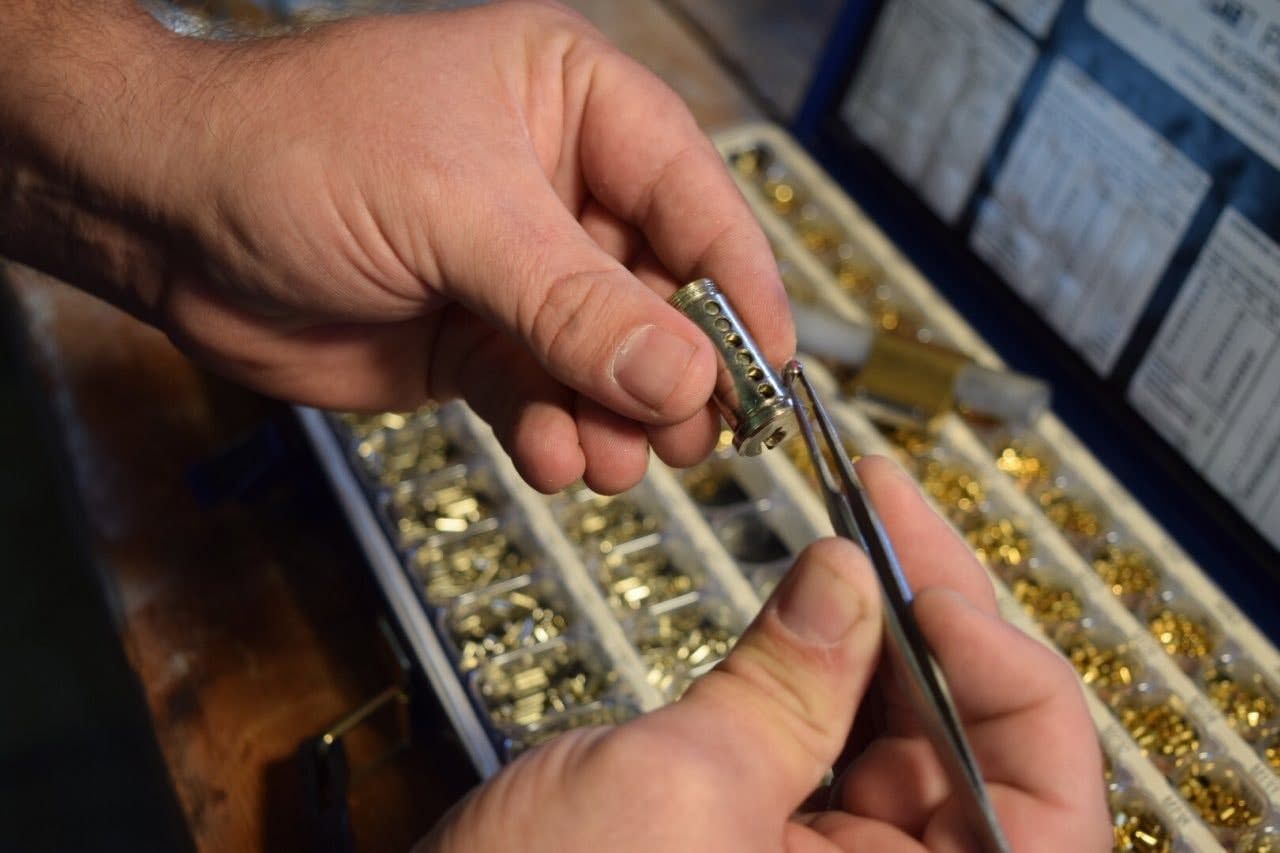 Hands sorting small jewelry pieces into trays with tweezers on a workbench