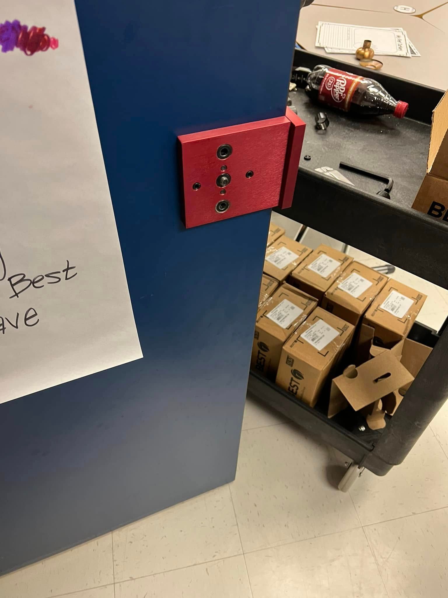 Red wall power outlet mounted on a blue panel beside shelves with boxes and bottles in a storage area