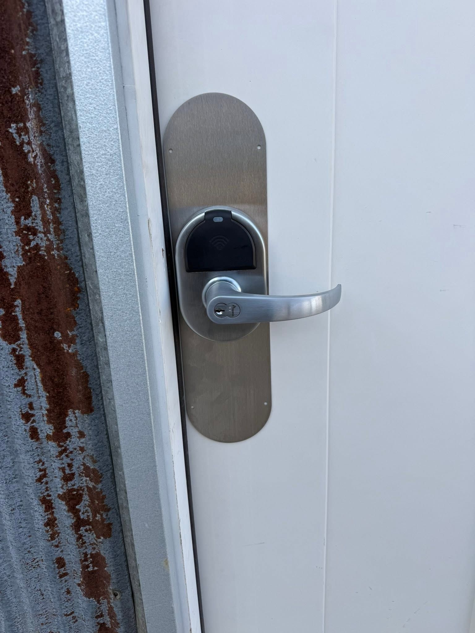 Close-up of a silver door handle and lock on a white door with a worn metal plate