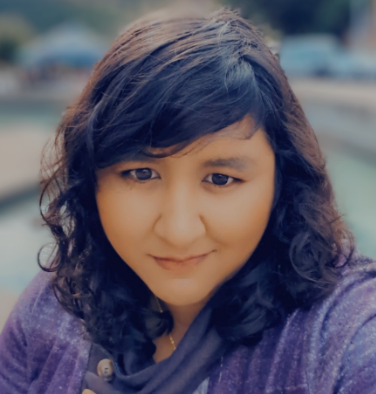 Close-up portrait of a smiling person in a purple sweater with a blurred outdoor background