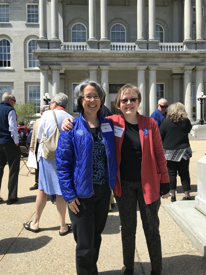 Two women in blue and red jackets posing outside a stone building