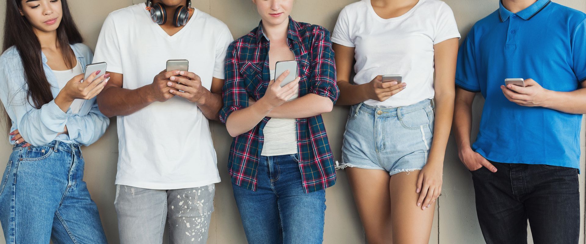A group of young people are standing next to each other looking at their phones.