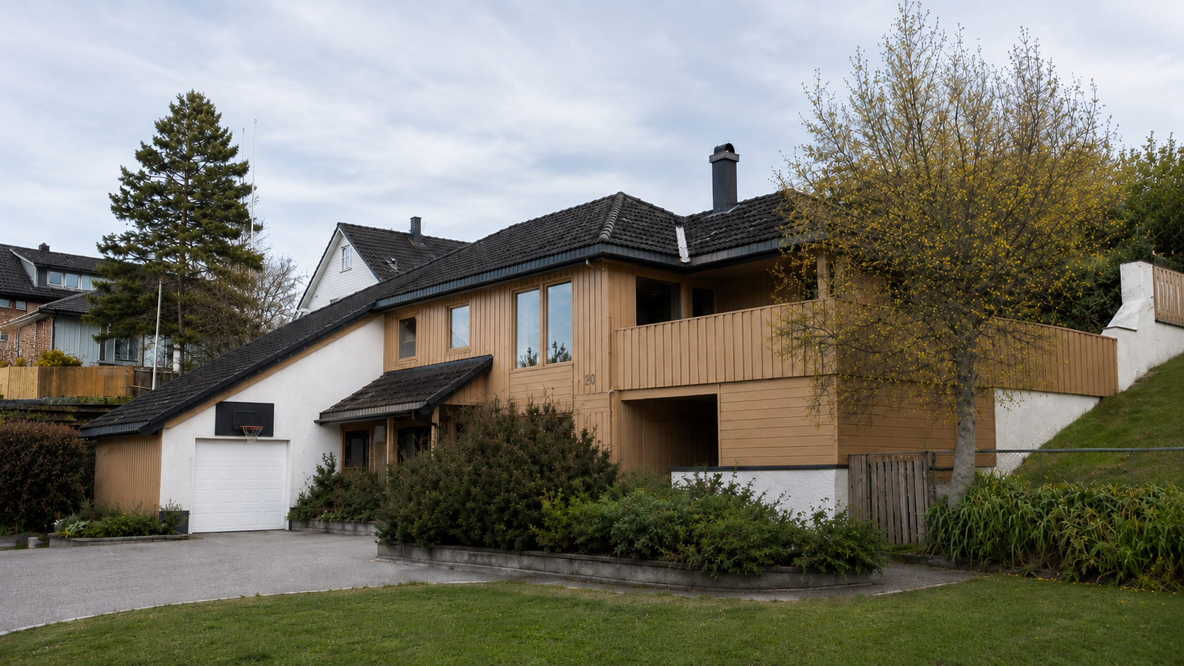 Moderne hus med brun treverk, mørkt tak og en plen foran ved siden av trær og busker