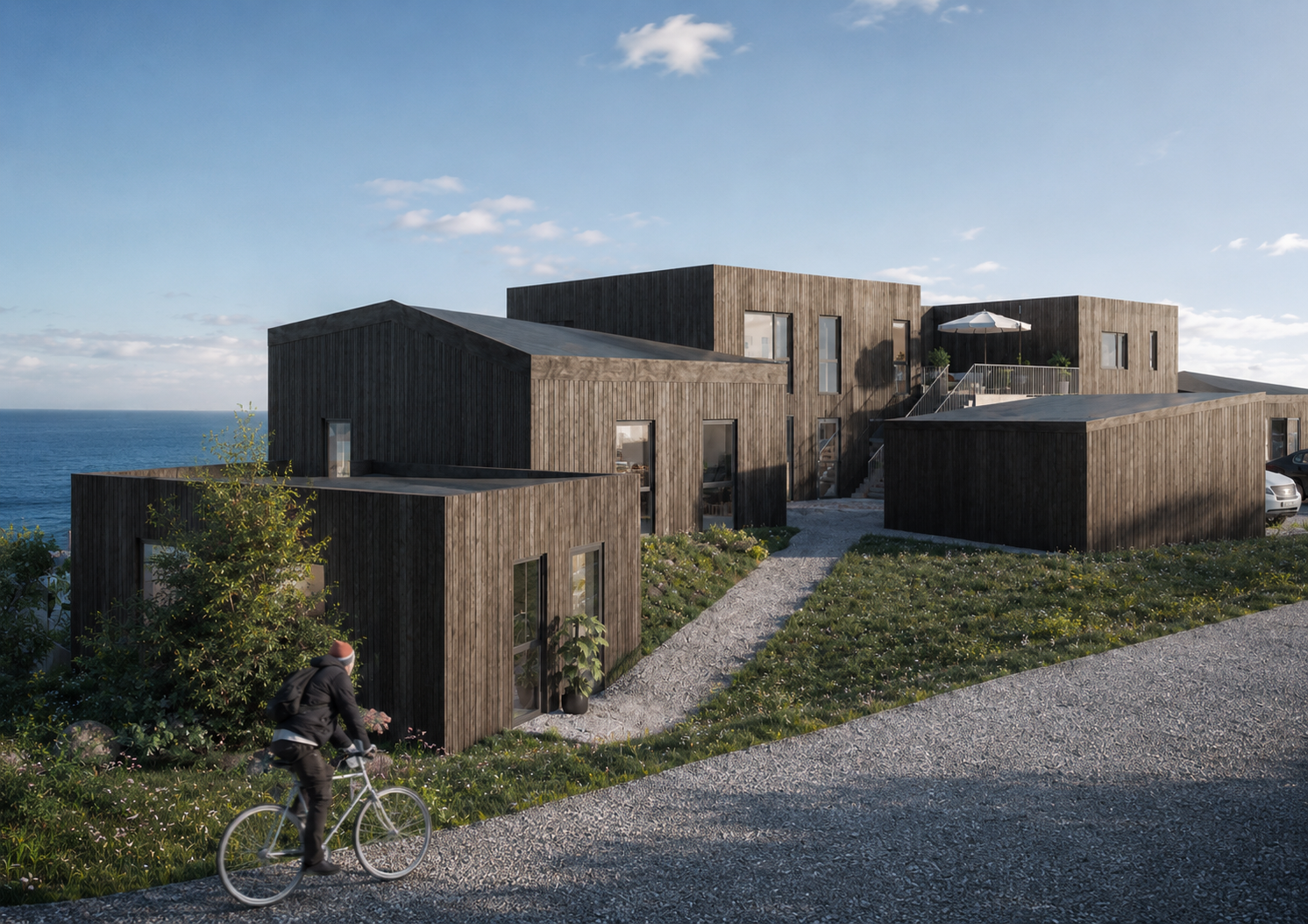 Moderne hus i en kyståsside, med en syklist på en grussti ved sjøen.