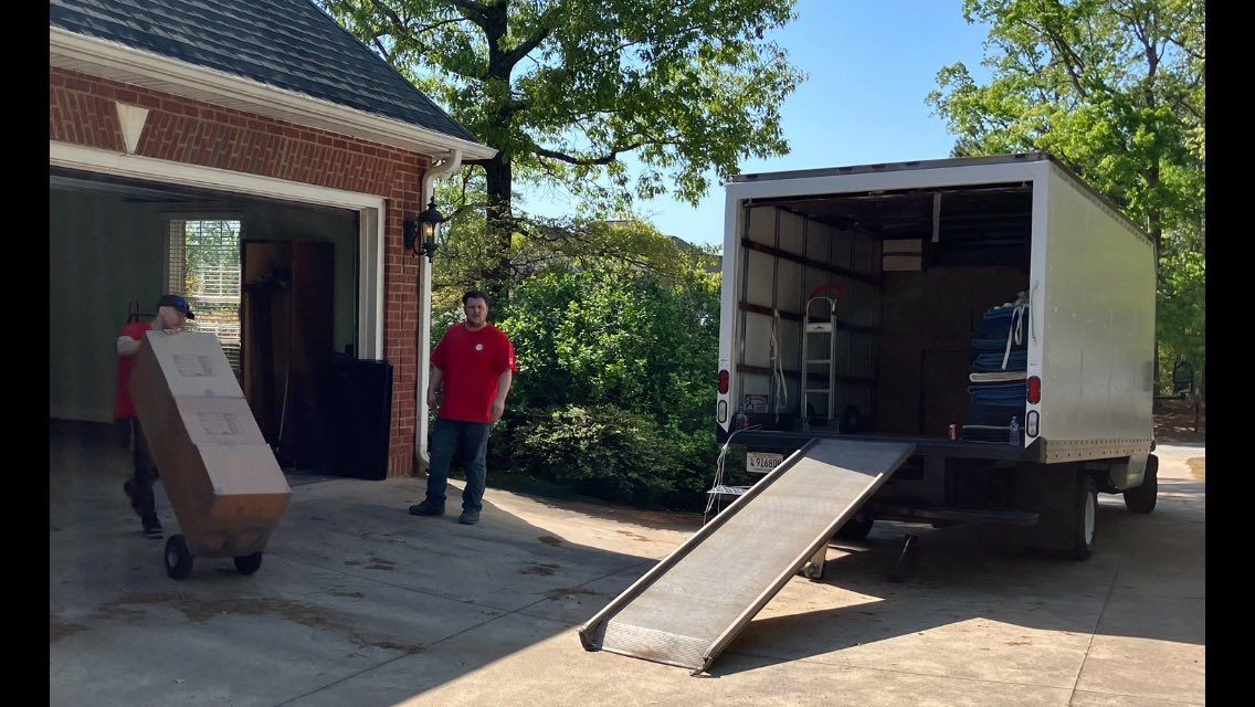 Two movers loading a box into a moving truck in front of a house.