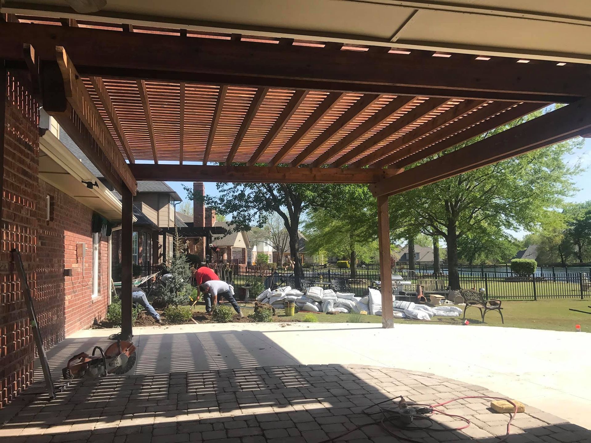 A person is standing under a wooden pergola in front of a brick house.