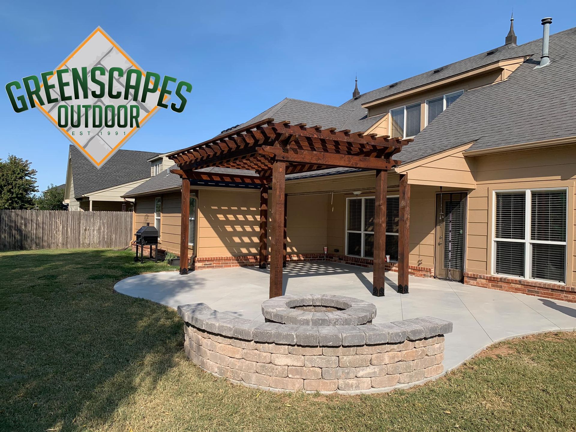 Backyard patio with pergola, fire pit, and house. Greenscapes Outdoor logo.