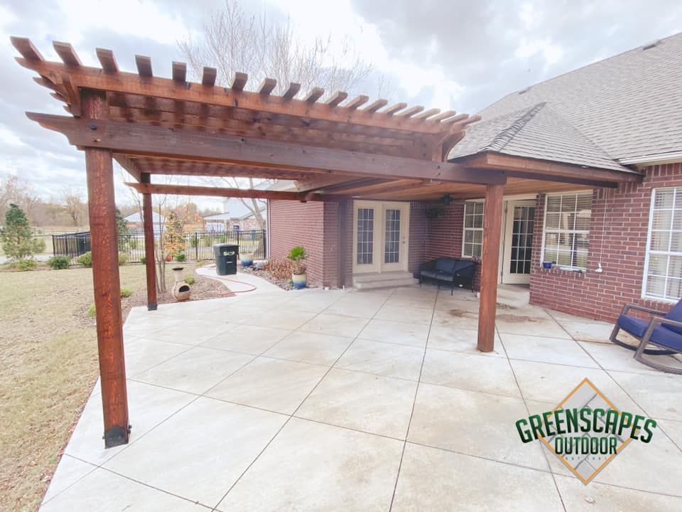 A wooden pergola is sitting on top of a patio in front of a brick house.