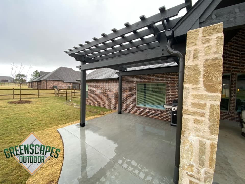 A pergola is sitting on top of a concrete patio next to a brick house.