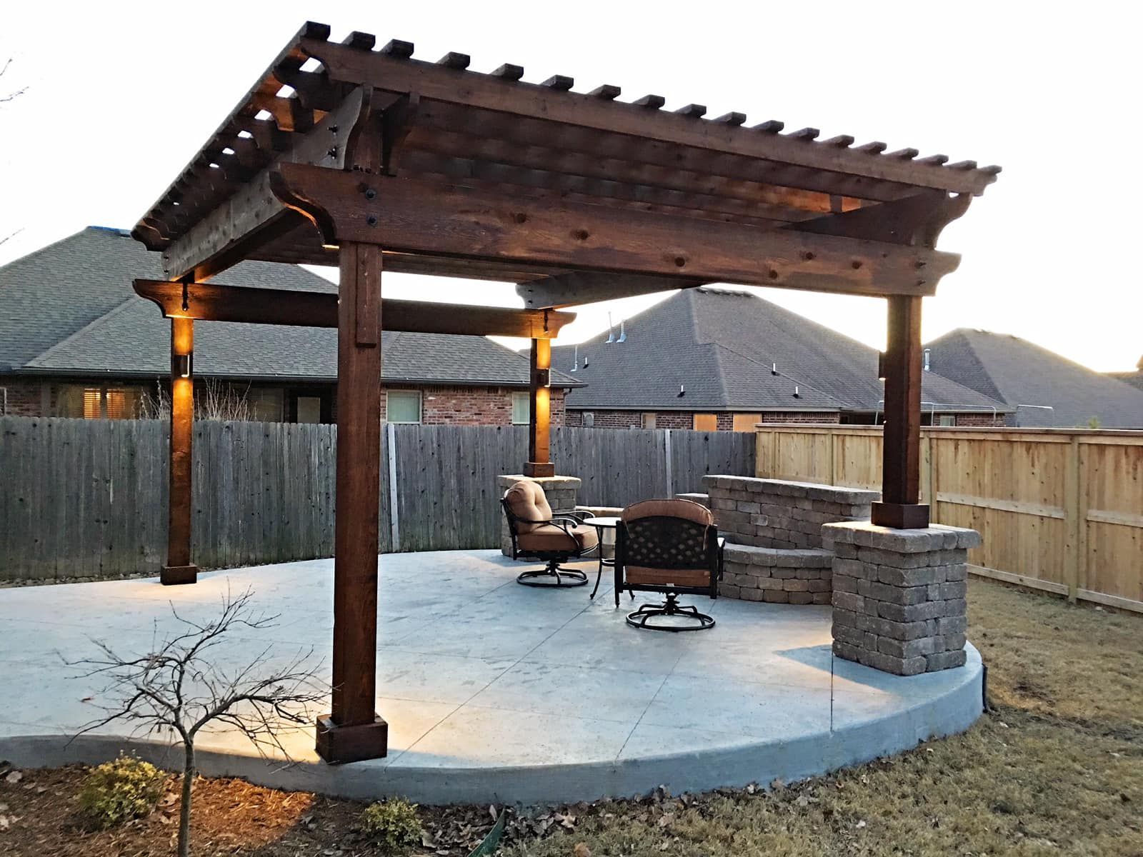 A wooden pergola with chairs and a fire pit in a backyard.