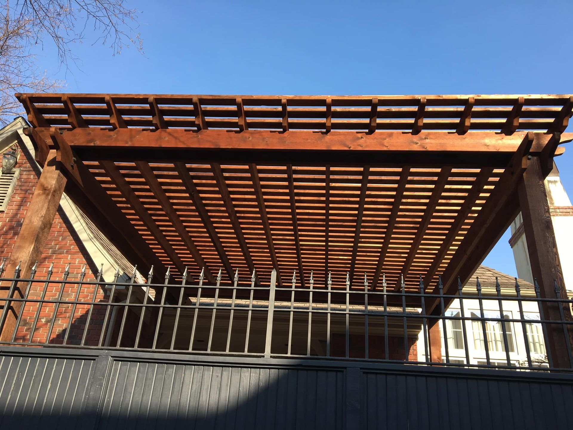 A wooden pergola is sitting on top of a metal fence.