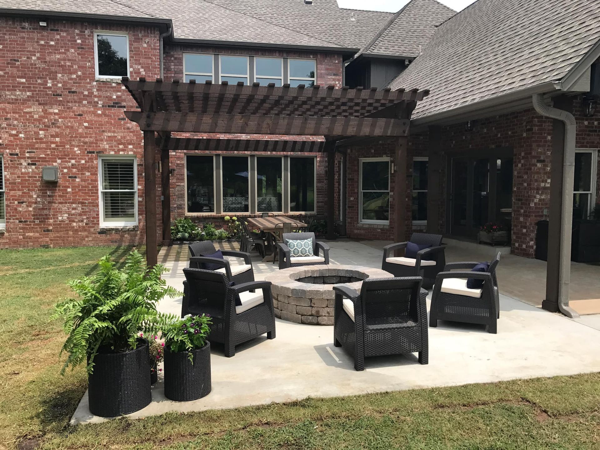 A patio with a fire pit and chairs under a pergola.