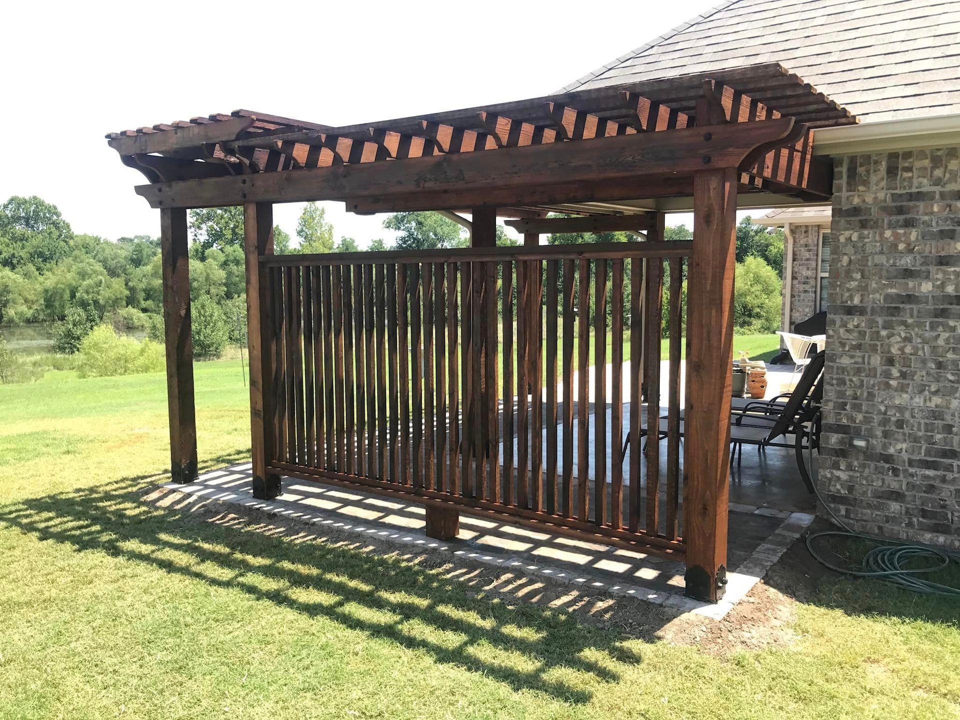 A wooden pergola is sitting in the grass next to a brick house.