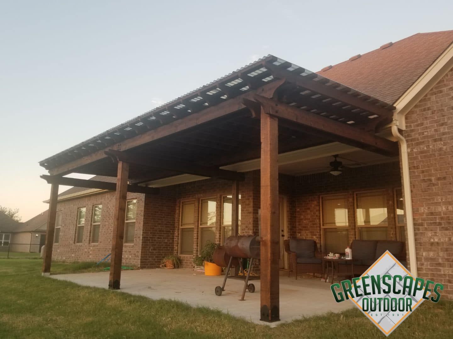 Wooden patio cover attached to a brick house, over a concrete patio with outdoor furniture.