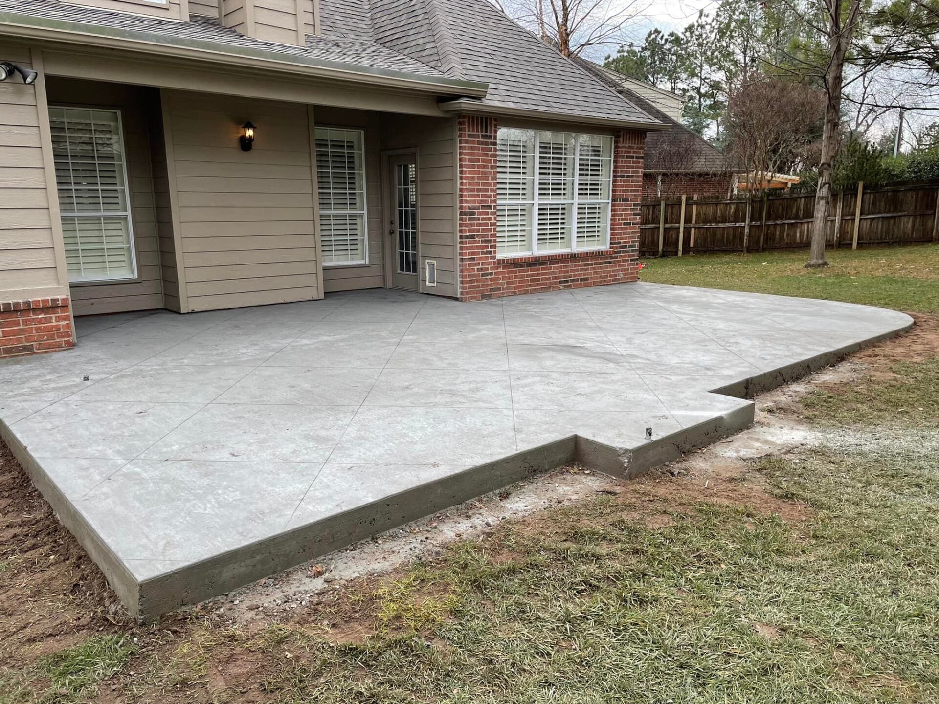 A concrete patio is being built in the backyard of a house.