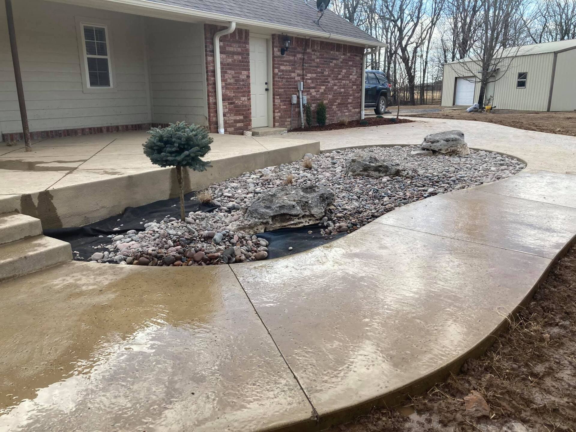 A concrete walkway leading to a house with a small tree in the middle.