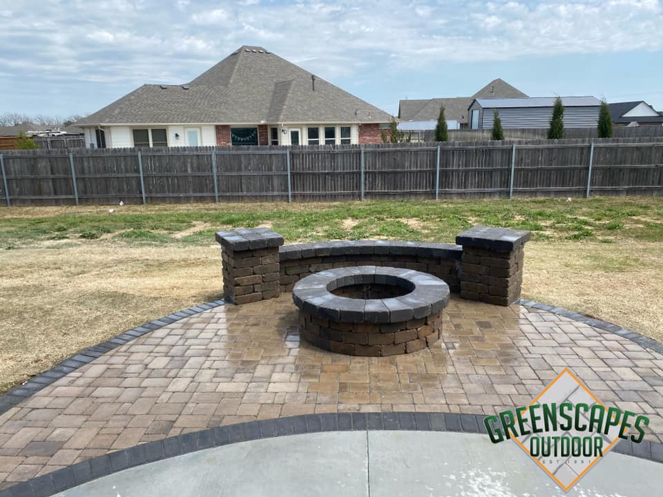 A fire pit is sitting on top of a brick patio in front of a house.